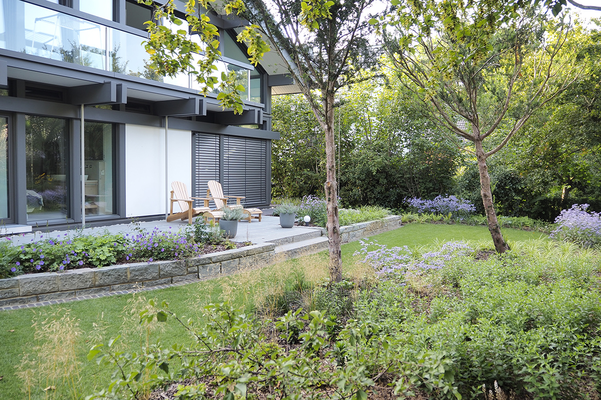  Im hinteren Gartenteil fängt ein Hochbeet mit Natursteinmauern den Höhenunterschied zum waldigen Gartenrahmen ab. Die bestehenden Eiben wurden aufgeastet und dürfen sich nun entwickeln.